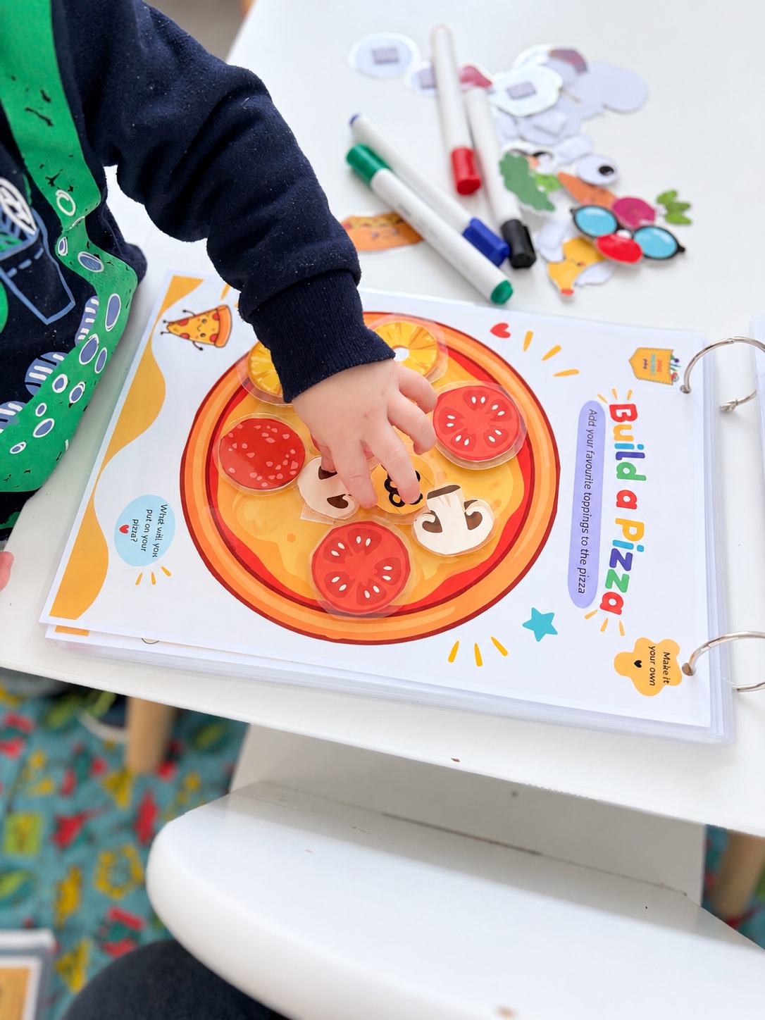 A toddler adding toppings to the Build a Pizza activity